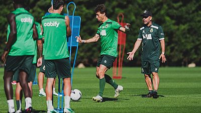 Íñigo Vicente practica control de balón en césped natural, supervisado por el entrenador José Alberto López. Chalecos con "cabify" y maniquíes de entrenamiento visibles.