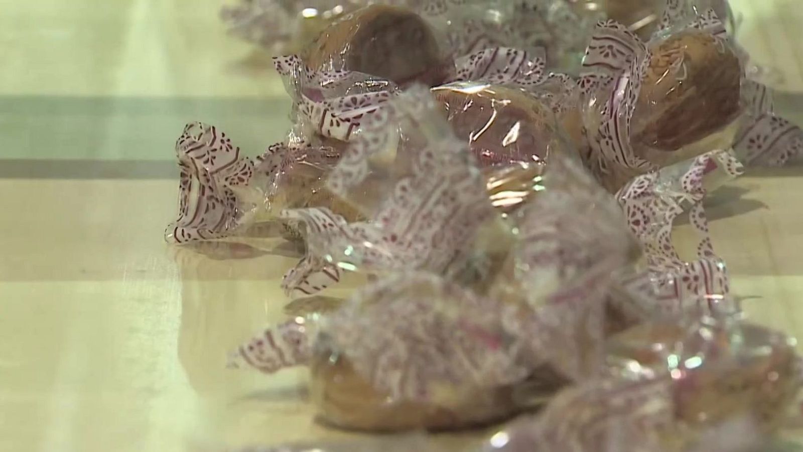 Primer plano de dulces envueltos individualmente con papel decorativo blanco y rojizo-púrpura sobre superficie reflectante.