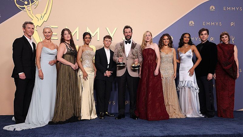 Un grupo de diez personas, cinco hombres y cinco mujeres, posan con trofeos dorados en los Premios Emmy. El fondo exhibe el logo de los Emmy, NBC y Peacock.