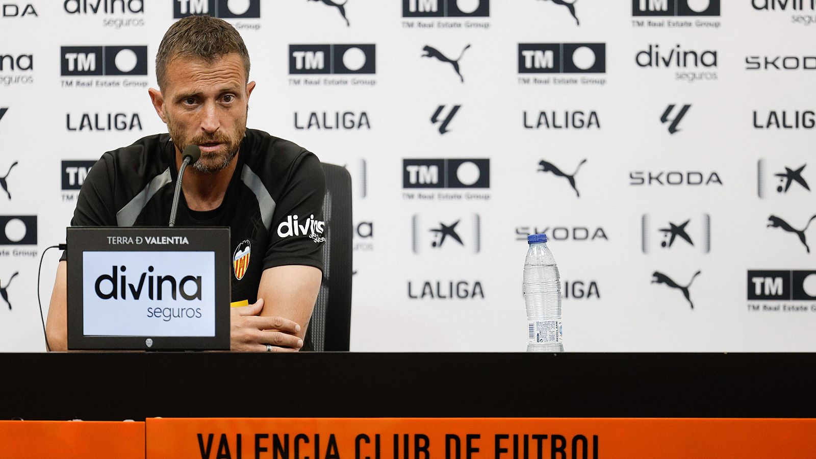 Rubén Baraja, entrenador del Valencia CF, en rueda de prensa. Viste camiseta negra con escudo del club y "divina seguros". Monitor con "TERRA D VALENTIA". Fondo de patrocinadores.