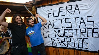 Pablo Fern�ndez Santos y Serigne Mbay� R�son, con pu�os en alto, sonr�en ante una pancarta antirracista. Una mujer con tambor visible a la izquierda.