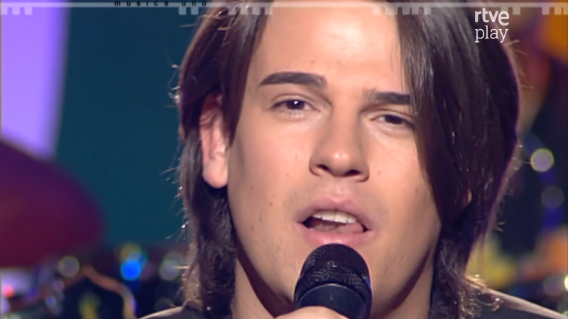 Raúl canta en un micrófono negro, con cabello largo y oscuro. "MUSICA UNO" y "rtve play" aparecen en el fondo de luces de colores.