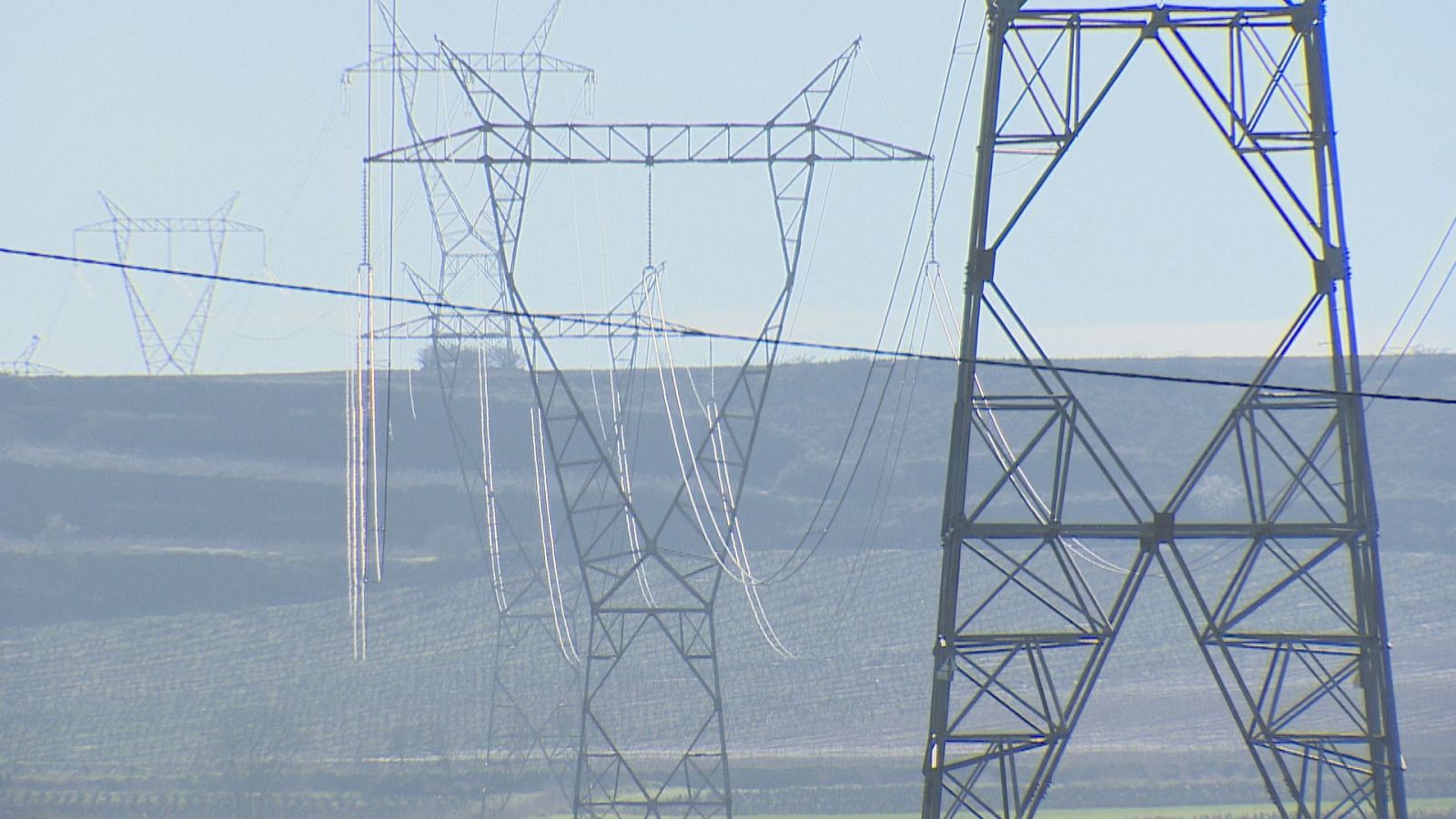 Paisaje con torres de alta tensión y cables eléctricos, destacando una estructura metálica robusta en primer plano y otras a lo lejos bajo un cielo despejado.