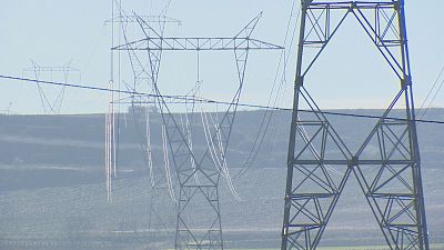 Paisaje con torres de alta tensi�n y cables el�ctricos, destacando una estructura met�lica robusta en primer plano y otras a lo lejos bajo un cielo despejado.