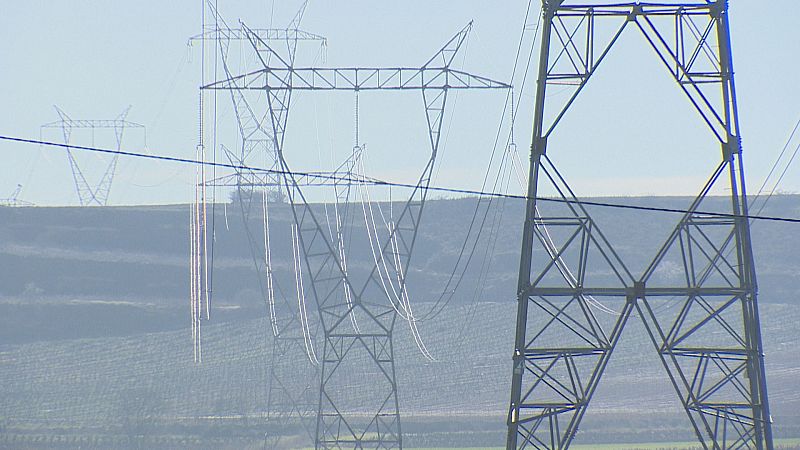 Paisaje con torres de alta tensión y cables eléctricos, destacando una estructura metálica robusta en primer plano y otras a lo lejos bajo un cielo despejado.