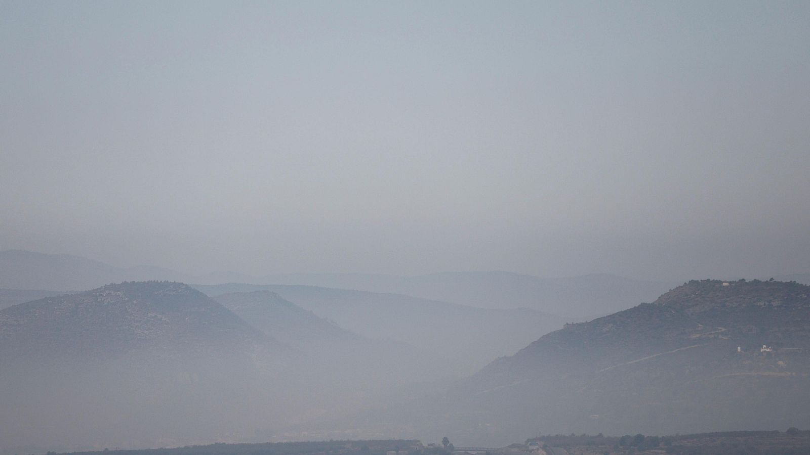 Paisaje montañoso brumoso con colinas en primer plano y montañas difuminadas al fondo. Atmósfera serena y melancólica con tonos apagados.