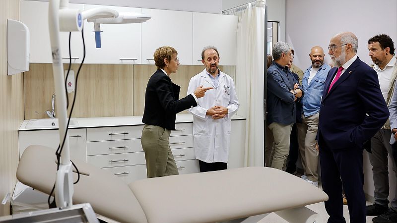 Miguel Sanz Sesma, expresidente de Navarra, observa una sala médica moderna donde una mujer explica el equipamiento a un médico. La escena sugiere una visita oficial a instalaciones sanitarias.