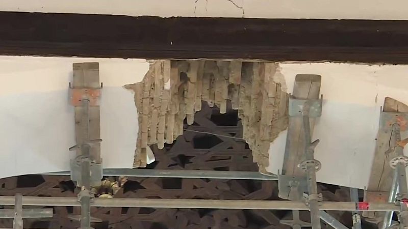 Techo interior dañado con viga de madera, superficie enlucida agrietada, listones de madera expuestos y andamio metálico debajo.