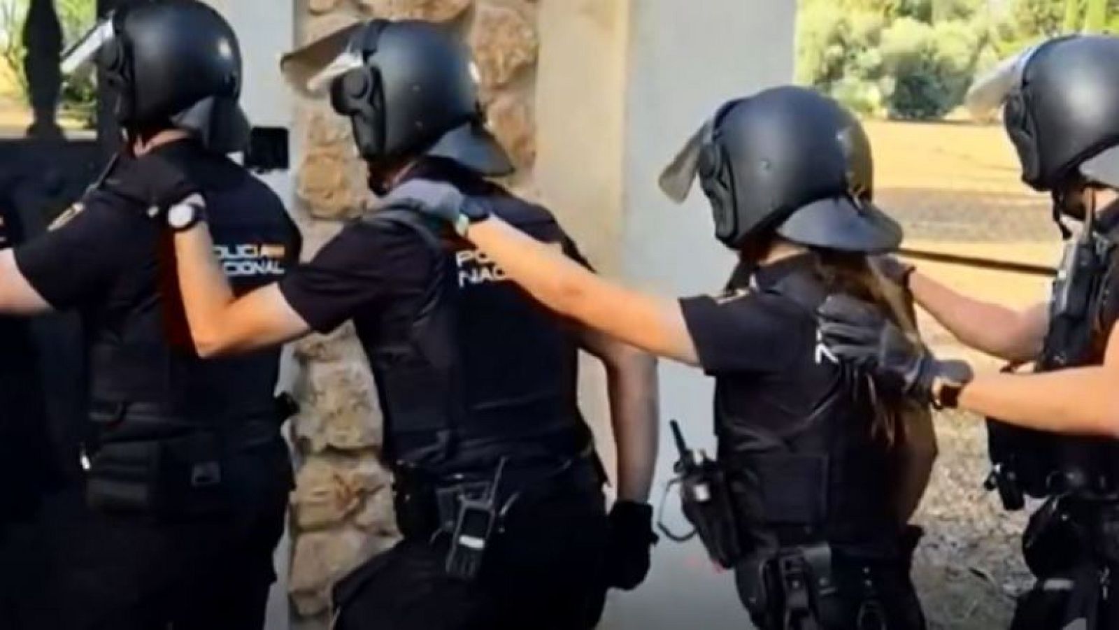 Agentes de la Policía Nacional de España, con uniformes tácticos y cascos, avanzan en formación. Se lee "POLICIA NACIONAL" en sus espaldas.