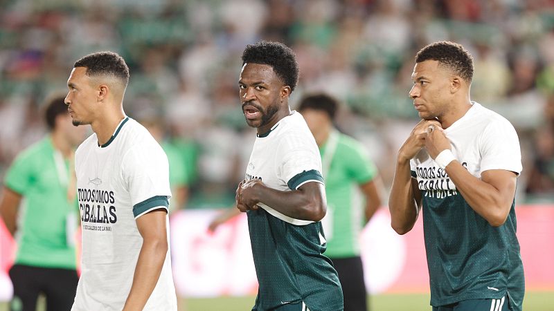 Tres hombres, uno de ellos Kylian Mbappé, posan con camisetas blancas que dicen "TODOS SOMOS CIBALAS" y un pez estilizado, en un estadio.