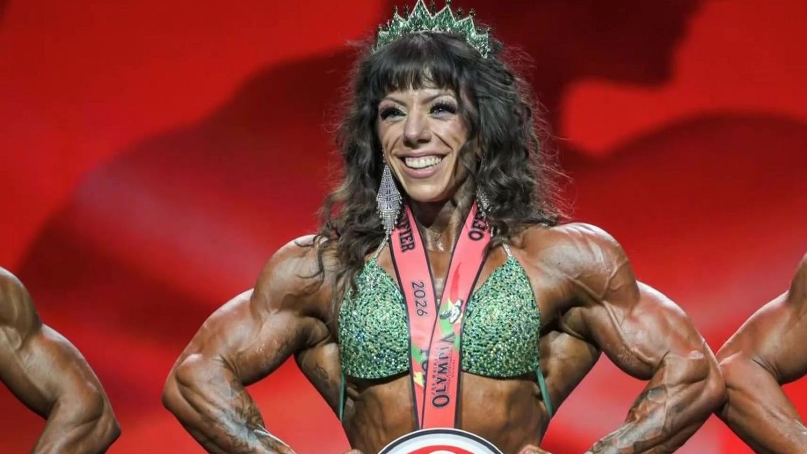 Culturista aragonesa Esther Cuartero, con bikini verde y corona, sonríe triunfalmente. Luce medalla "QUALIFIER OLYMPIA 2026".