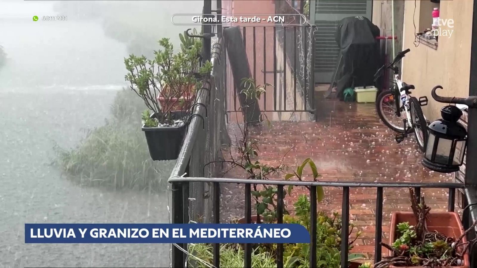 Tormenta de lluvia y granizo en Girona. Se observa una terraza con barandilla, plantas, bicicleta y mobiliario exterior. El fondo muestra vegetación borrosa por la lluvia. Logo de rtve play y titular sobre el Mediterráneo.