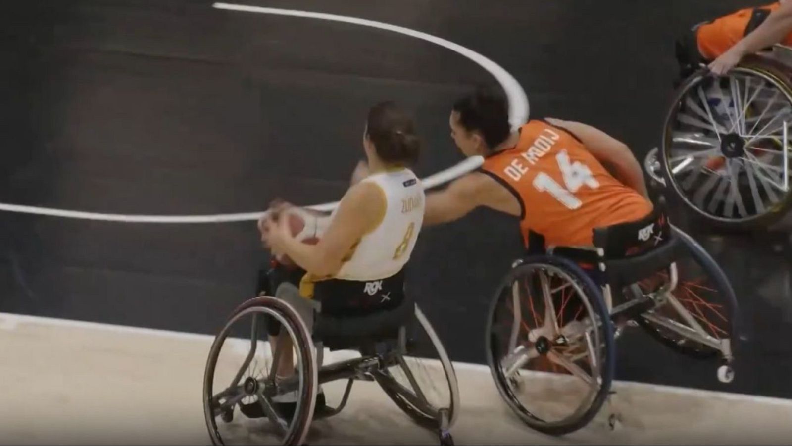 Jugadoras de baloncesto en silla de ruedas compiten por el balón. Una viste camiseta blanca con el número 8 "RGX", la otra naranja con "DE MOOIJ 14".