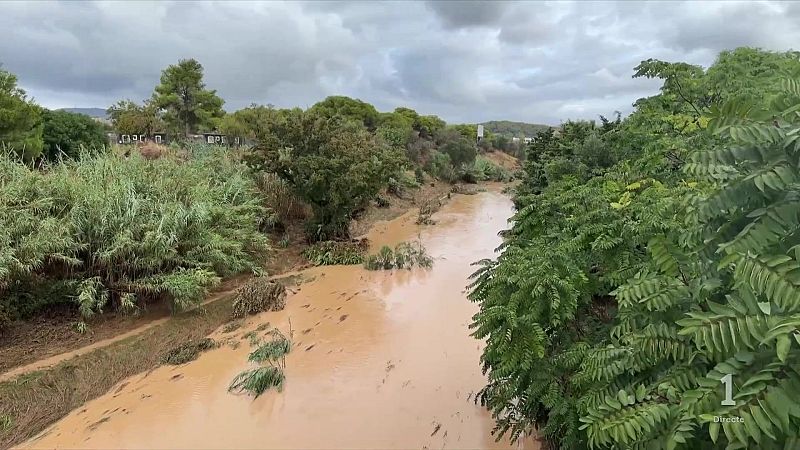 Río crecido y turbio con vegetación exuberante en las orillas. Gráfico de televisión indica "1 Directe" en la esquina inferior derecha.