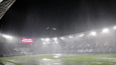 Estadio de f�tbol de noche con lluvia intensa. Pantalla LED anuncia suspensi�n del partido. Se lee "LEVANTE 1909" en las gradas. Campo mojado con charcos.