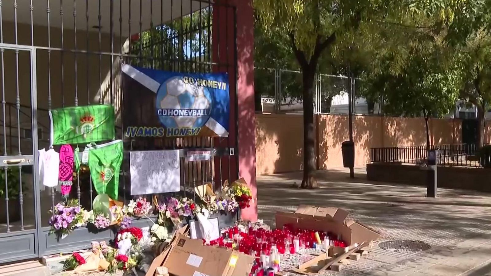 Memorial con flores, velas y banderas del Real Betis Balompié y una pancarta dedicada a "Honey", en un espacio público.