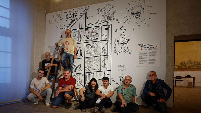 Grupo de personas posando frente a un mural de cómic en blanco y negro con el título "Faltabezes & Kanpai Jotze & Kolektiboa".