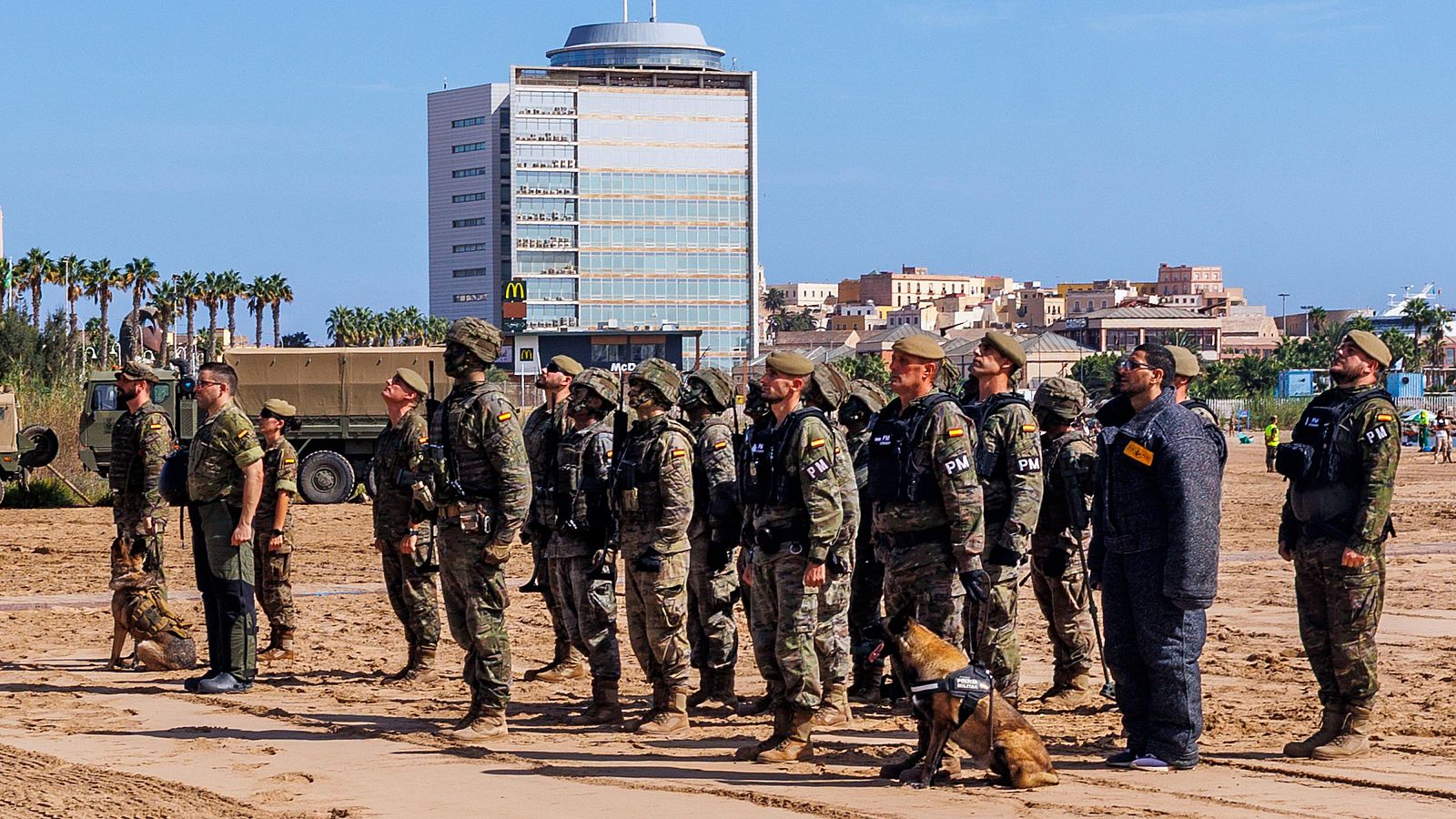Militares españoles con perros de trabajo y un camión militar frente a un edificio moderno con el logo de McDonald's en Melilla.