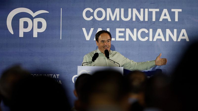 Carlos Mazón, con el pulgar hacia arriba, sonríe mientras habla en un evento del Partido Popular en la Comunitat Valenciana. El logo del PP es visible en el fondo.