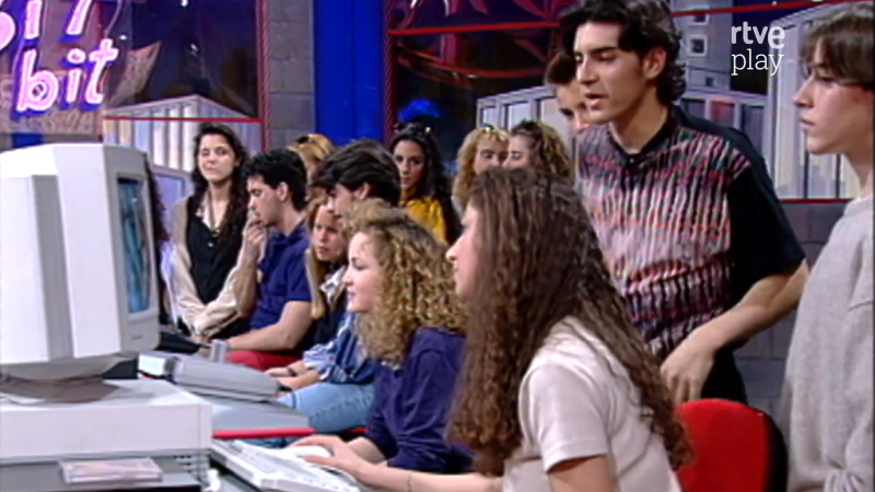 Jóvenes interactúan con un ordenador CRT en un plató de televisión con el letrero "Bit a bit" y el logo "rtve play".
