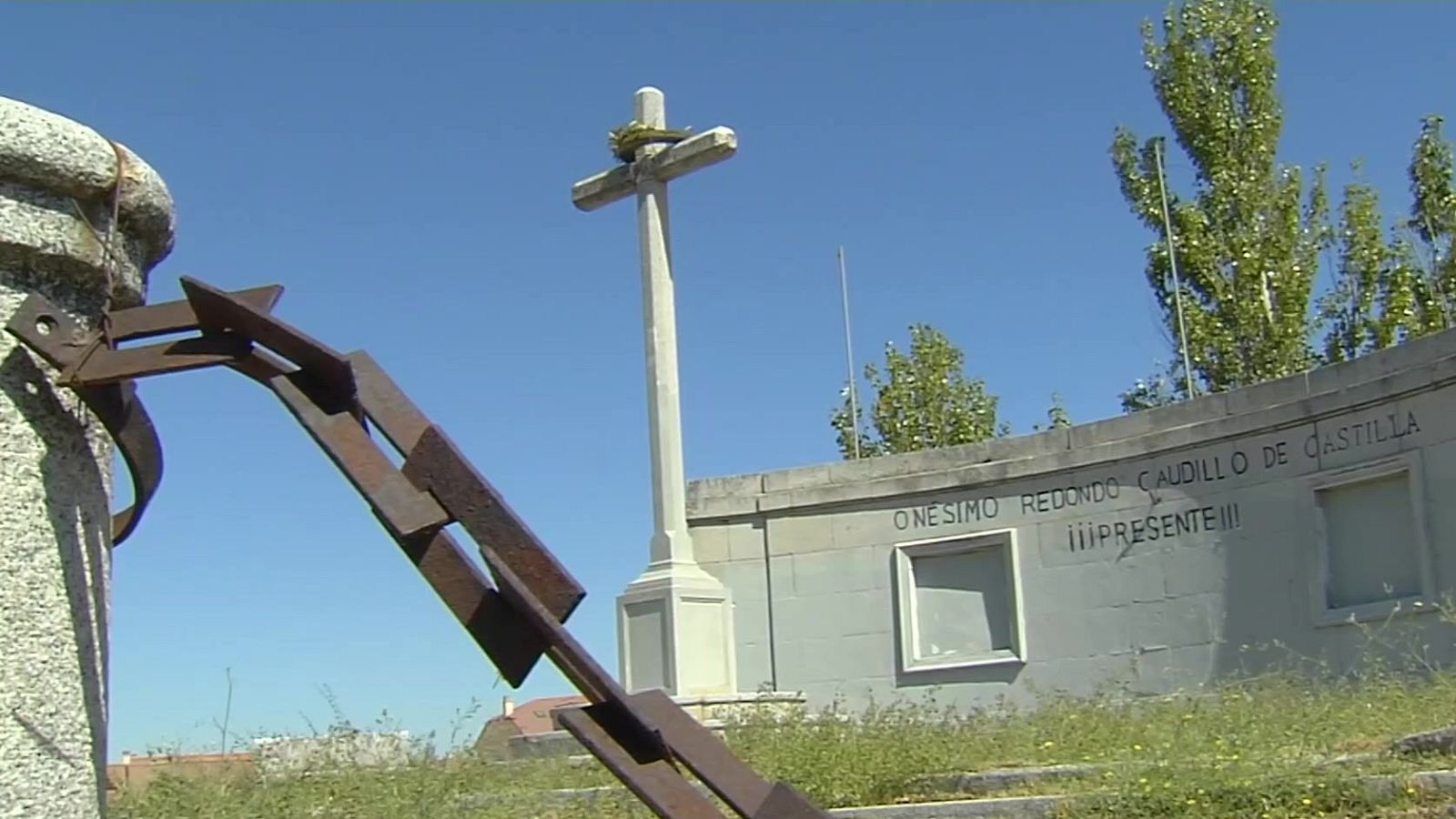 Monumento a Onésimo Redondo con cruz de piedra, pedestal, muro semicircular y la inscripción "ONESIMO REDONDO CAUDILLO DE CASTILLA ¡¡¡PRESENTE!!!" bajo un cielo azul.