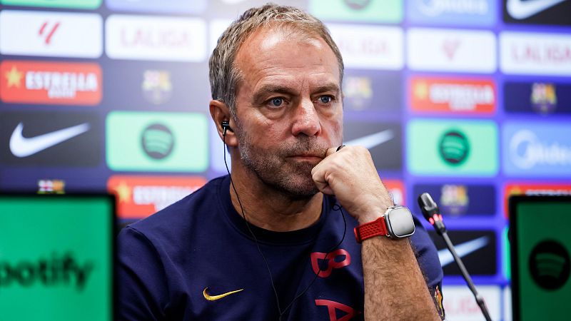 Primer plano de Hansi Flick en rueda de prensa, con sudadera "BARÇA" y logos de patrocinadores detrás, incluyendo "Spotify" y "LALIGA".