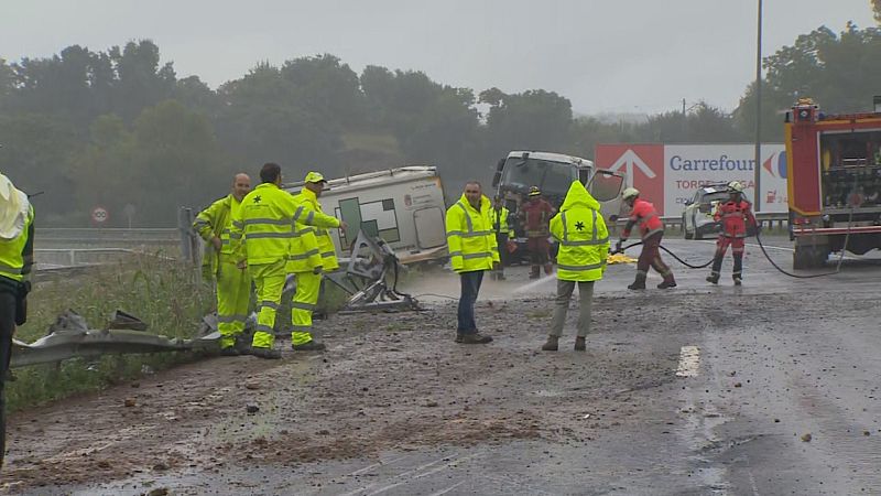 Accidente en carretera mojada: vehículo de emergencia volcado, bomberos actuando y personal de servicios de emergencia en acción. Se observa un cartel de Carrefour y Torrejón de Ardoz al fondo.