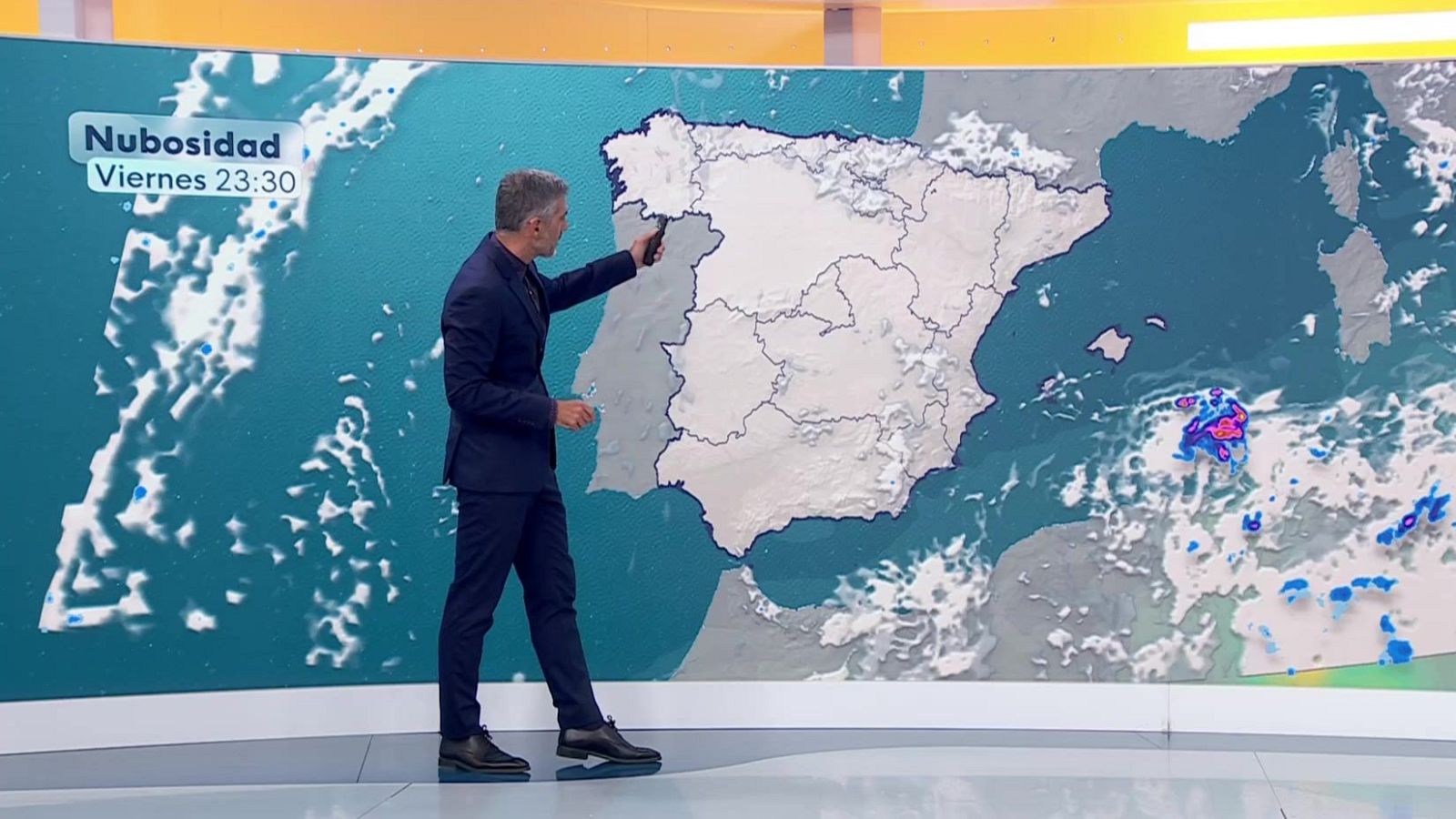 Roberto Brasero presenta el pronóstico del tiempo en televisión, señalando un mapa de España y Portugal con nubosidad y precipitaciones para el viernes a las 23:30.