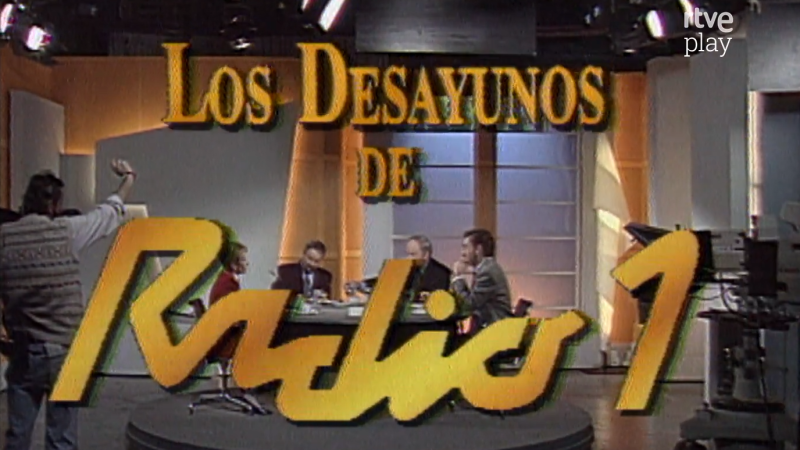 Estudio de TV con logo "Los Desayunos DE Radio 1", debate con Luis Mariñas y otros dos hombres, persona de espaldas, decorado retro y logo "tve play".