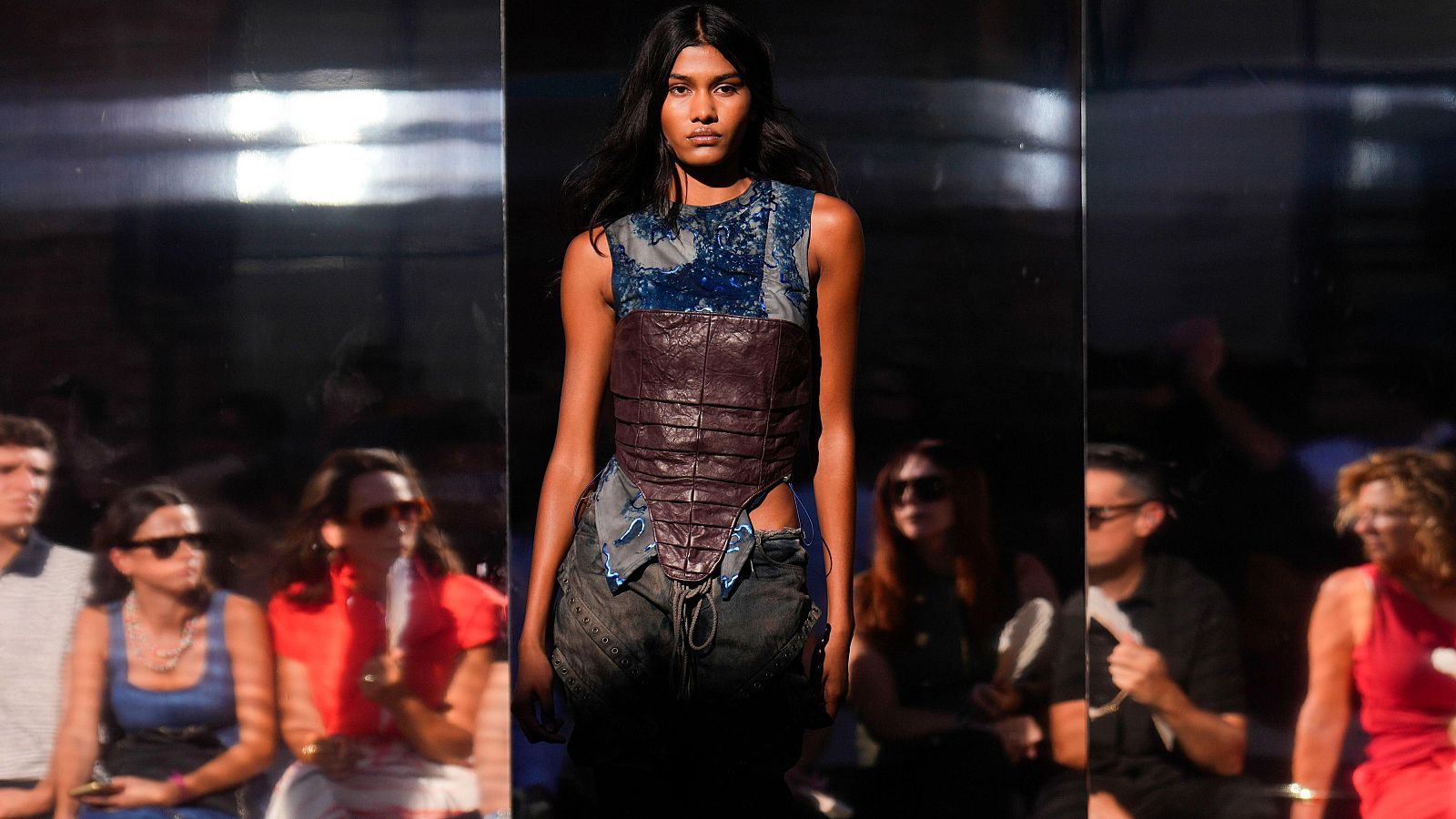 Karla Aguilar desfila en la Mercedes-Benz Fashion Week Madrid con un top asimétrico y pantalones cargo oscuros. El fondo reflectante y la iluminación la destacan en la pasarela.
