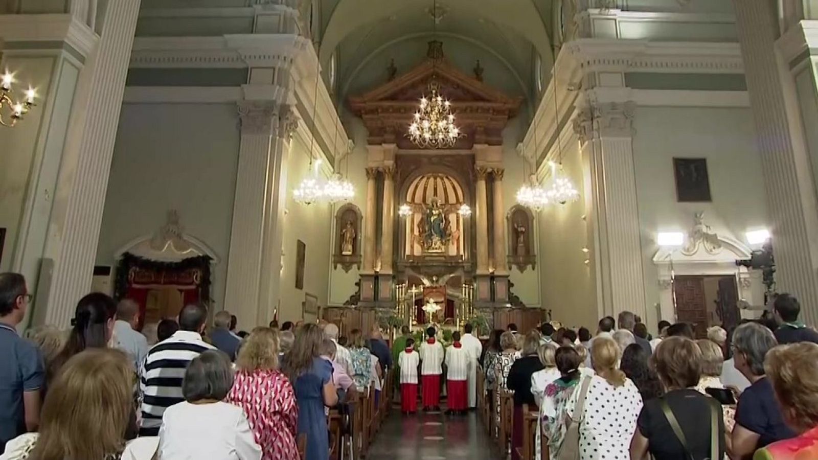 Interior de una iglesia con altar mayor, retablo, estatua de la Virgen María, congregación y clero en servicio religioso.