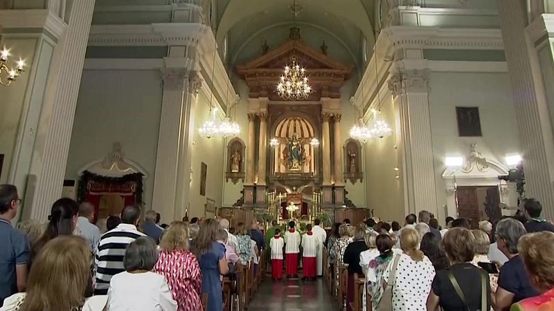 Interior de una iglesia con altar mayor, retablo, estatua de la Virgen María, congregación y clero en servicio religioso.