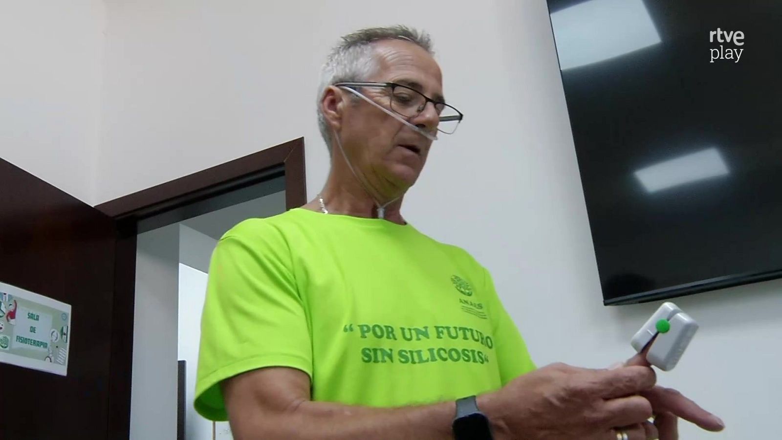 Hombre con cánula nasal y oxímetro en sala de fisioterapia, viste camiseta "POR UN FUTURO SIN SILICOSIS" UGT FICA. Logo RTVE Play en esquina superior derecha.