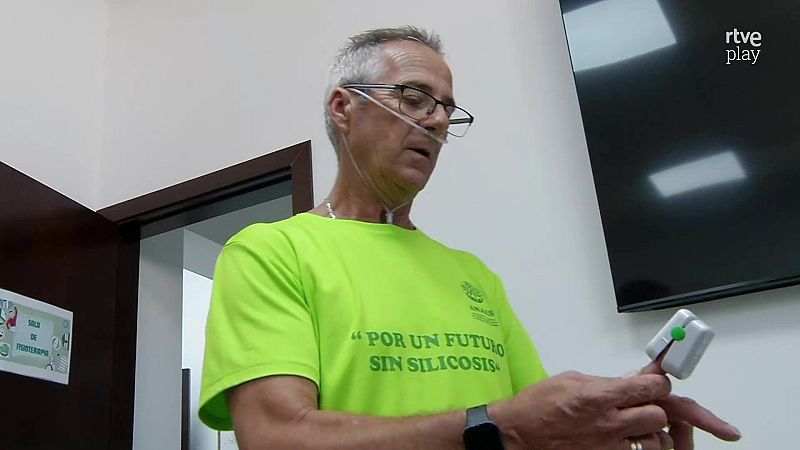 Hombre con cánula nasal y oxímetro en sala de fisioterapia, viste camiseta "POR UN FUTURO SIN SILICOSIS" UGT FICA. Logo RTVE Play en esquina superior derecha.