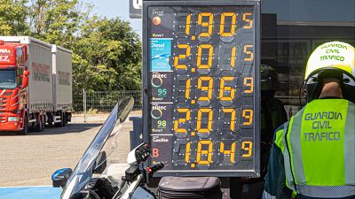 Panel de precios de combustible en gasolinera espa�ola: Diesel 1.905, Diesel NEXIA 2.015, efitec 95 1.969, efitec 98 2.079, Gas�leo B 1.849 ?/l. Agente Guardia Civil Tr�fico presente.