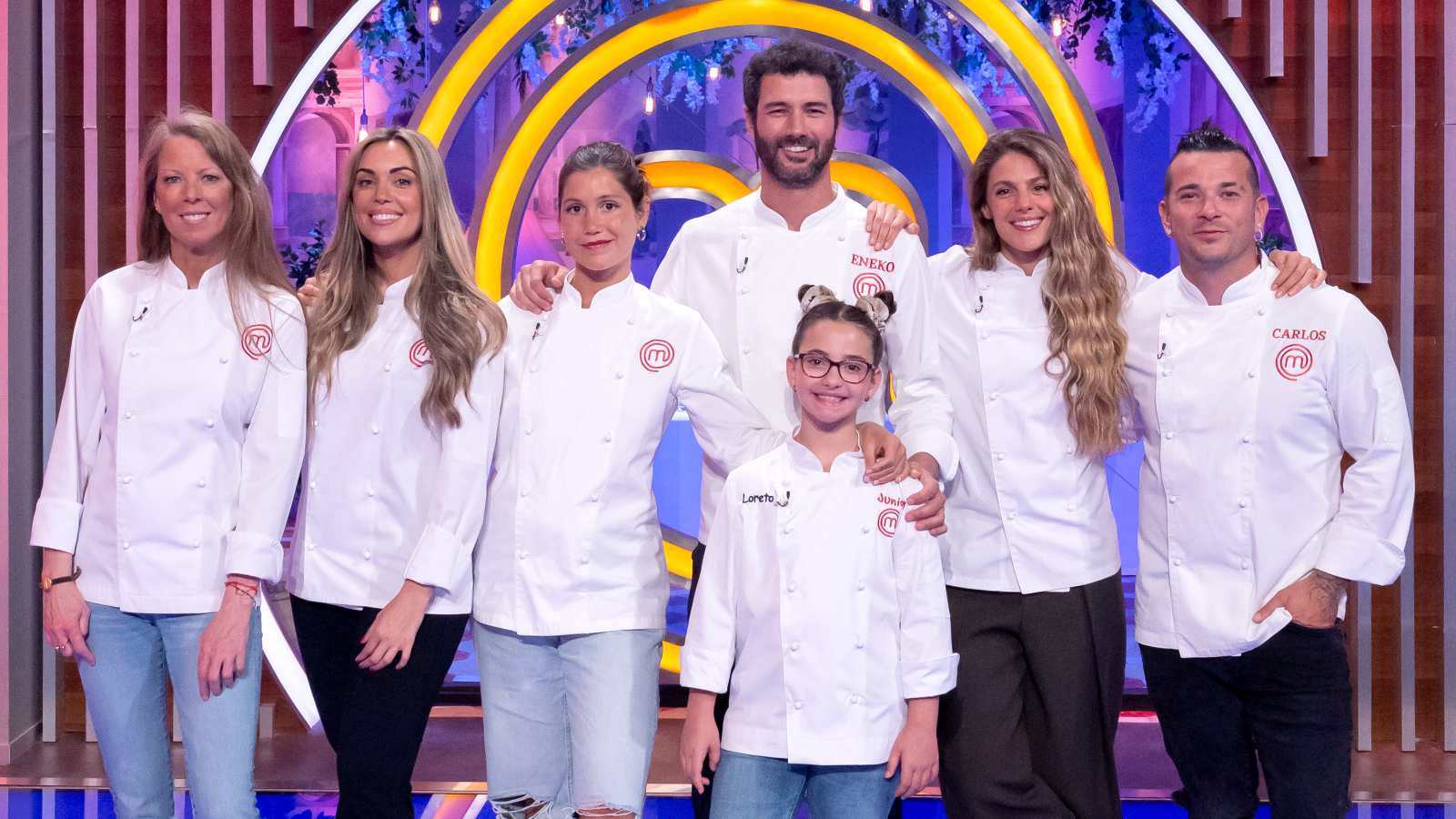 Loreto, Marta Verona, Eneko y Carlos Maldonado posan con otros dos adultos en un plató de MasterChef, luciendo chaquetillas de chef blancas y sonrisas.
