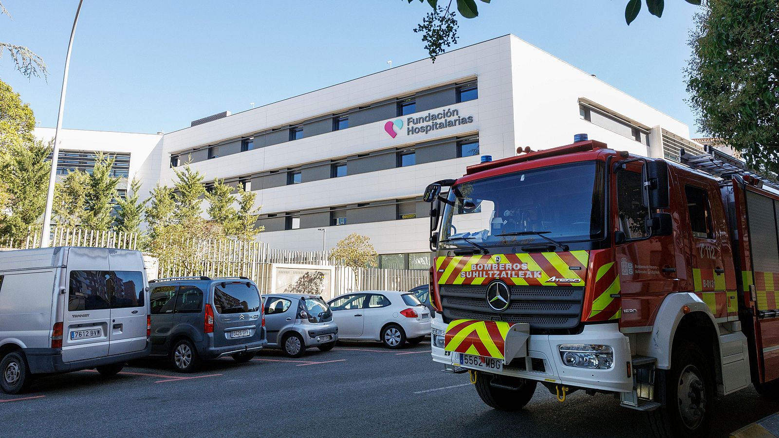 Edificio blanco "Fundación Hospitalarias" con camión de bomberos rojo "BOMBEROS SUHILTZAILEAK" y vehículos aparcados.
