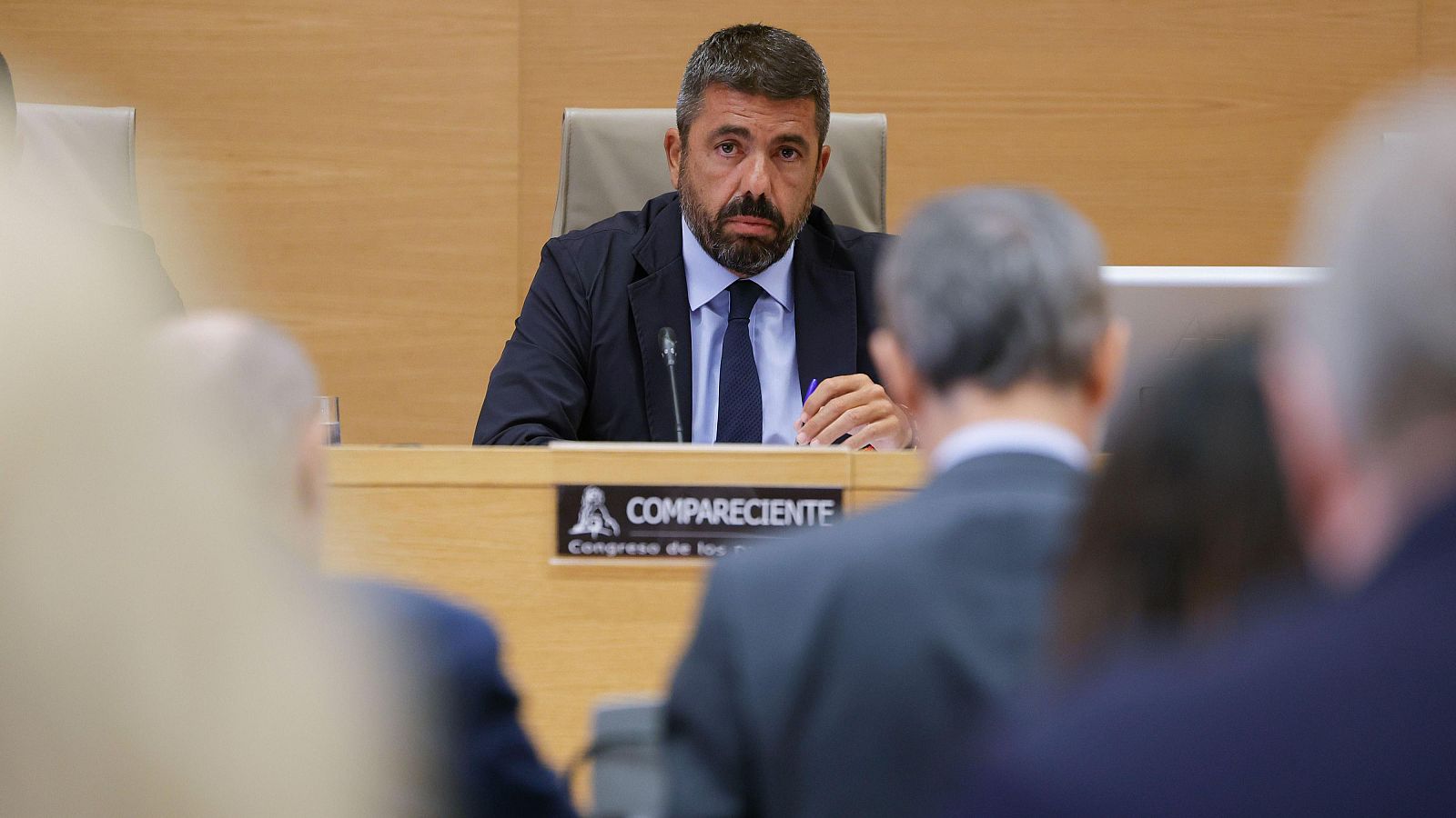 Óscar Puente, Ministro de Transportes, en el Congreso de los Diputados. Lleva traje oscuro, camisa azul y corbata azul oscuro. Sostiene un bolígrafo morado sobre el atril.