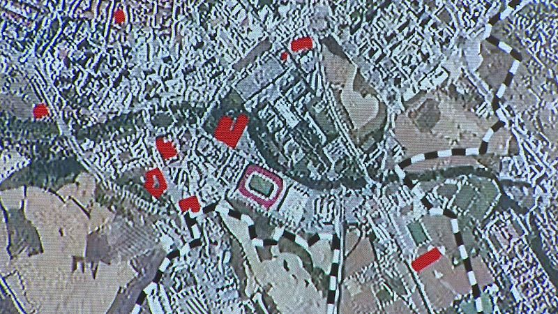 Mapa digital de Pamplona con áreas edificadas, zonas verdes y puntos rojos. Destaca el Estadio El Sadar y una línea discontinua que atraviesa el trazado urbano.