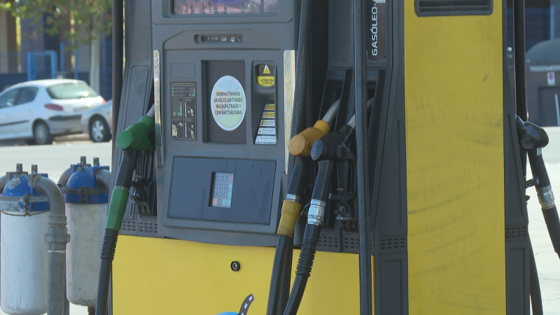 Primer plano de un surtidor de gasolina gris y amarillo con "GASÓLEO" vertical. Pantalla digital muestra "0.00" en tres líneas. Mangueras con boquillas de colores verde, amarillo, negro.