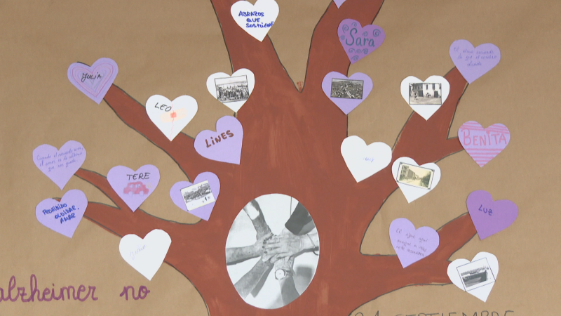 Árbol de papel con corazones de recuerdos, nombres y frases sobre el Alzheimer, adornado con fotos antiguas. En el tronco, manos unidas; abajo, "alzheimer no" y "21 SEPTIEMBRE".