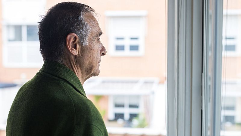 Primer plano de un hombre mayor de perfil, mirando por una ventana. Viste cárdigan verde oscuro. Se aprecian detalles de su rostro y el exterior desenfocado.