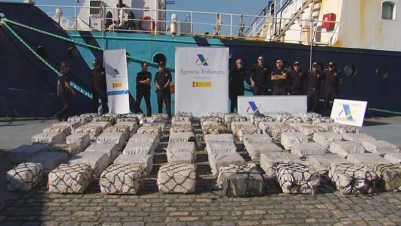 Decenas de fardos de droga incautados, custodiados por agentes uniformados de la Agencia Tributaria y Aduanas en un muelle portuario.