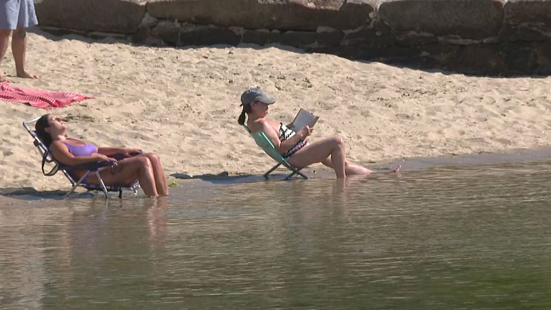 Mujeres en sillas de playa en la orilla, una leyendo y otra descansando, en un día soleado.