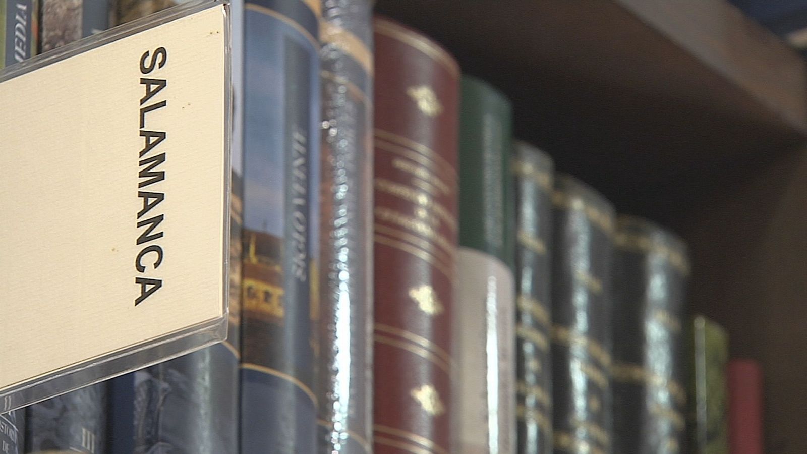 Estantería de madera oscura con libros antiguos de encuadernaciones variadas y detalles dorados. Etiqueta "SALAMANCA" en primer plano.