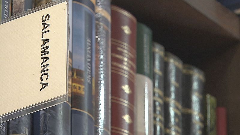 Estantería de madera oscura con libros antiguos de encuadernaciones variadas y detalles dorados. Etiqueta "SALAMANCA" en primer plano.