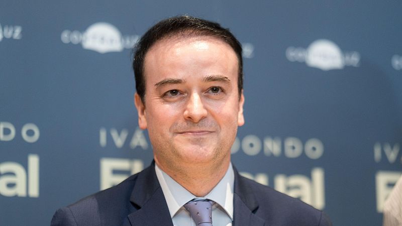 Luis Planas, Ministro de Agricultura, Pesca y Alimentación, en un primer plano con traje azul oscuro. Fondo azul con textos "IVA" y "Fondo Rural" inferidos.