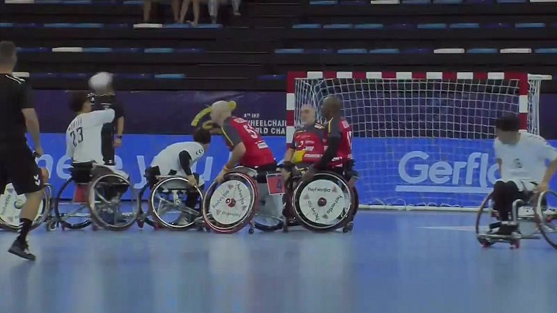Jugadores de balonmano en silla de ruedas compiten en una cancha azul, vistiendo camisetas blancas y rojas. Se aprecian vallas publicitarias y la porter�a.