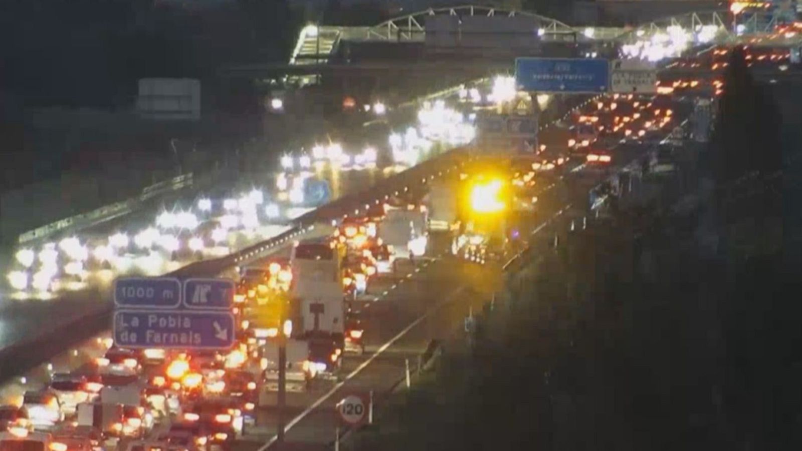 Tráfico nocturno intenso en autopista cerca de La Pobla de Farnals, con señal de 120 km/h y luz amarilla intermitente. Contexto: DIA SIN COCHES, L'informatiu - Comunitat Valenciana.