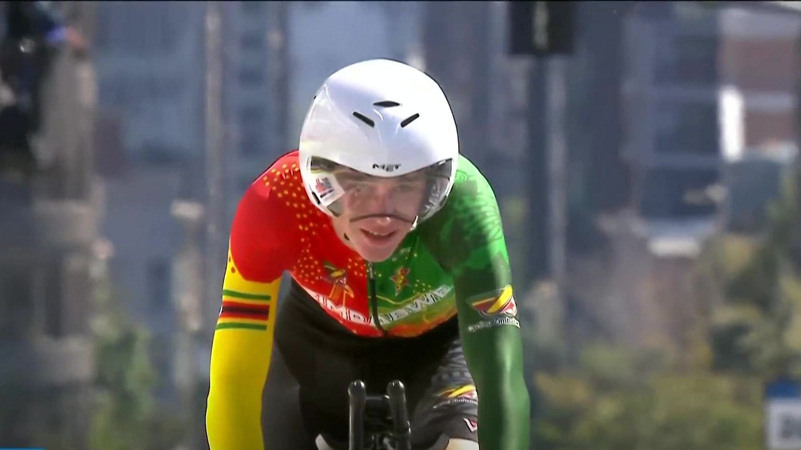 Ciclista con casco MET y mono de Zimbabue, concentrado en competición. Se aprecian detalles del emblema del pájaro y la palabra "ZIMBABWE" en su indumentaria.
